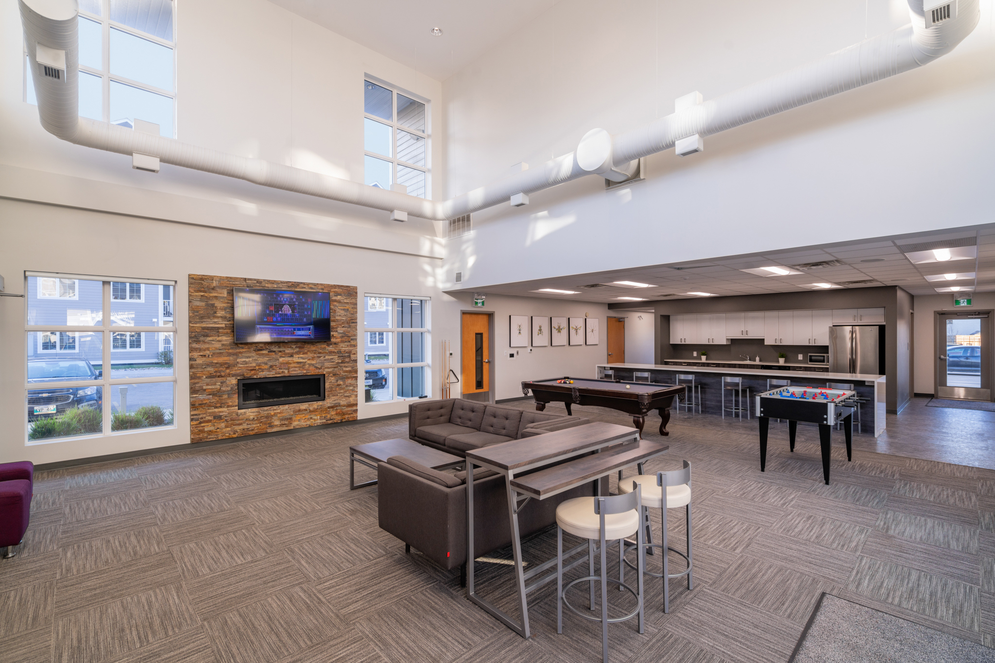 Image of the lobby area, showing couches, a pool table, a foosball table, a tv, fireplace and a kitchen area.