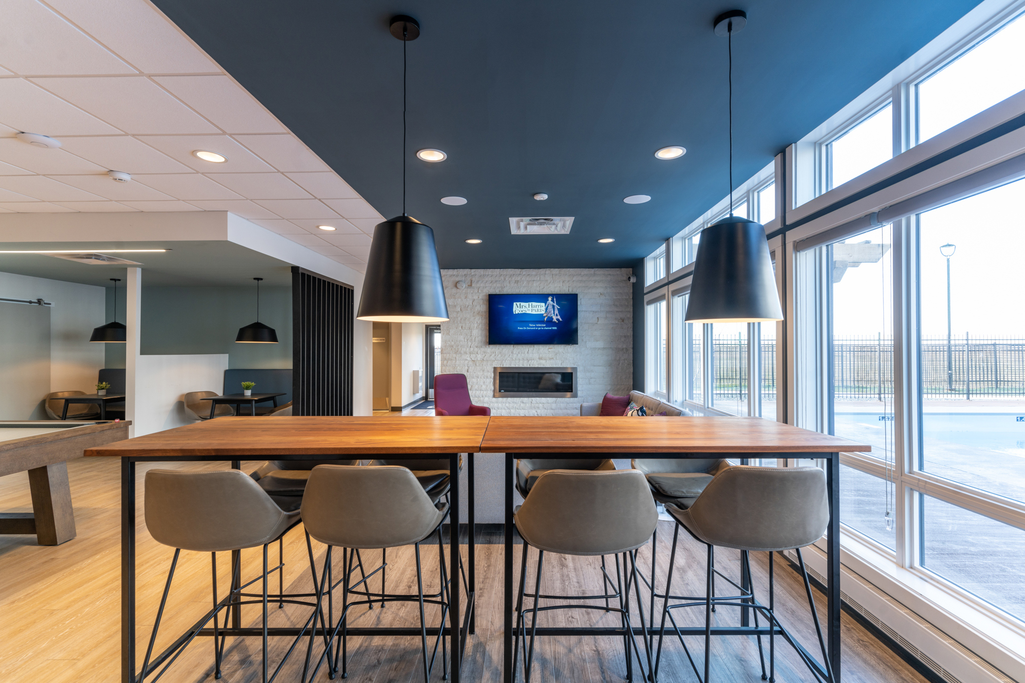 Image inside of the lounge of the building, with booth seating, a table with chairs, couches, an electronic fireplace, a tv and a pool table.