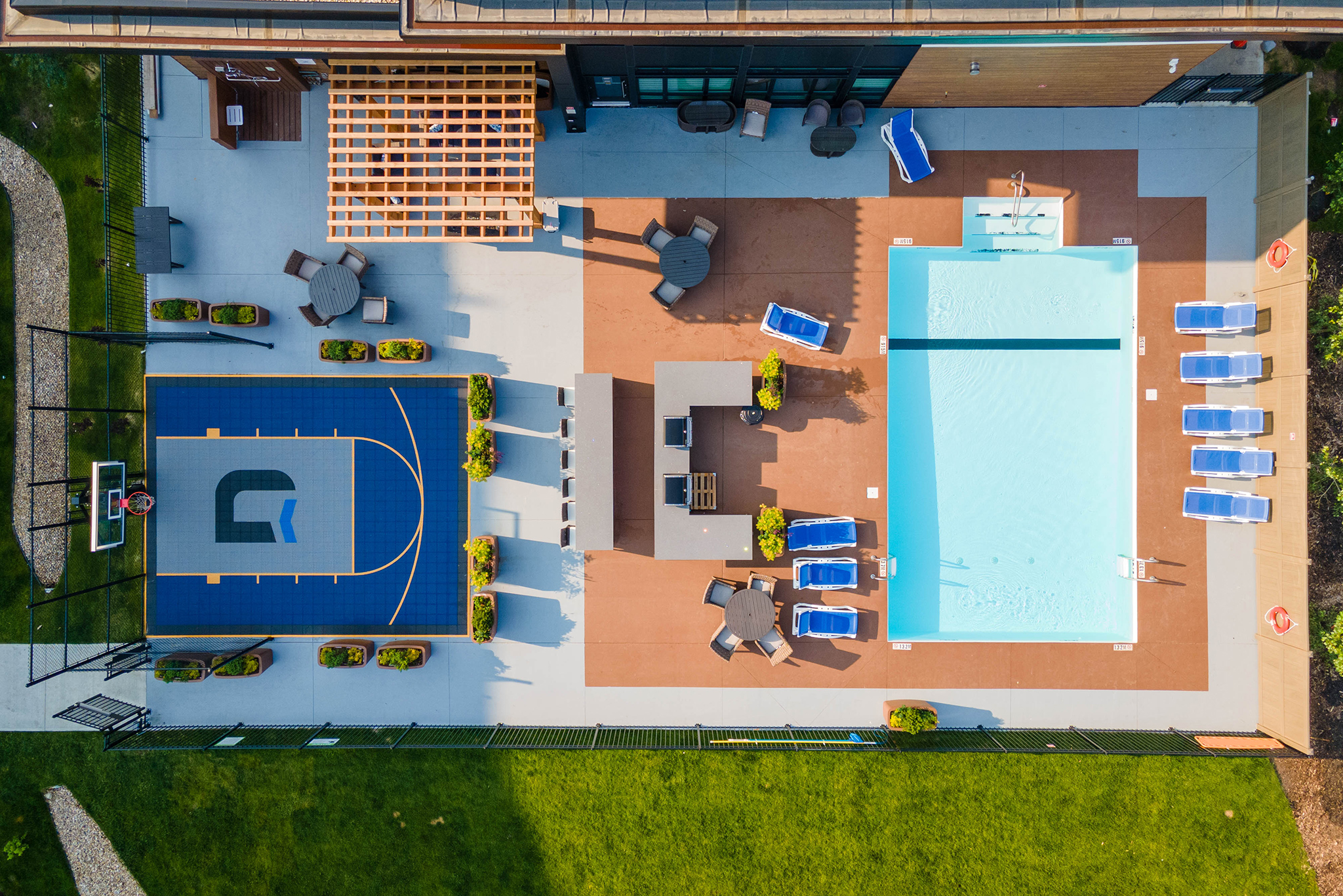 Top down image of an exterior courtyard, which shows a pool with chairs, a basketball court and patio seating.