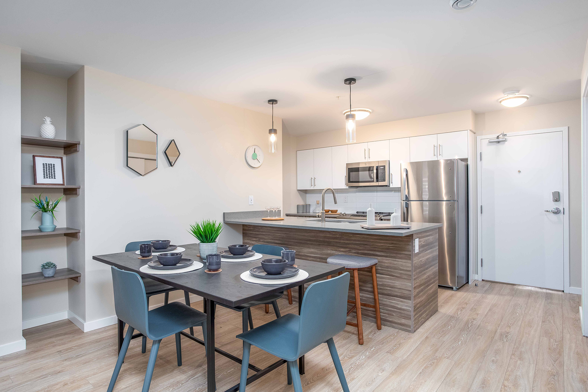 Image of the kitchen and dining area of a suite. There is a dark table with blue chairs and a wooden island with a granite countertop.