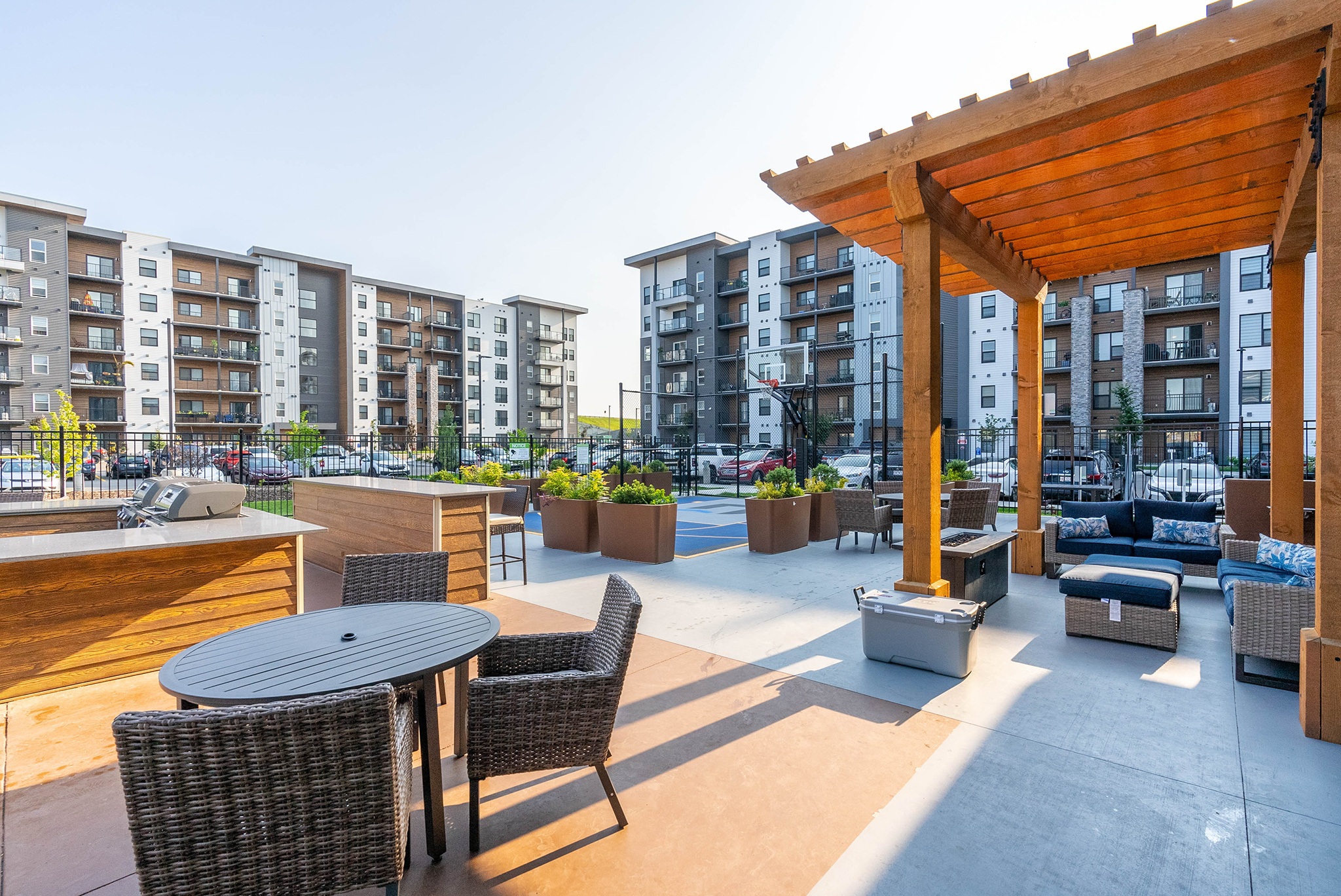 Image of an exterior courtyard, showing patio seating and tables, as well as planters and barbecues.