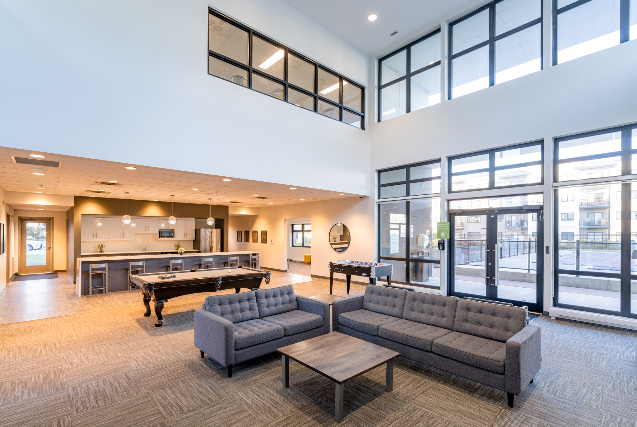 Image inside the lobby of the apartment block. There are couches, a large island with chairs, a fridge and a sink. There is also a pool and foosball table.