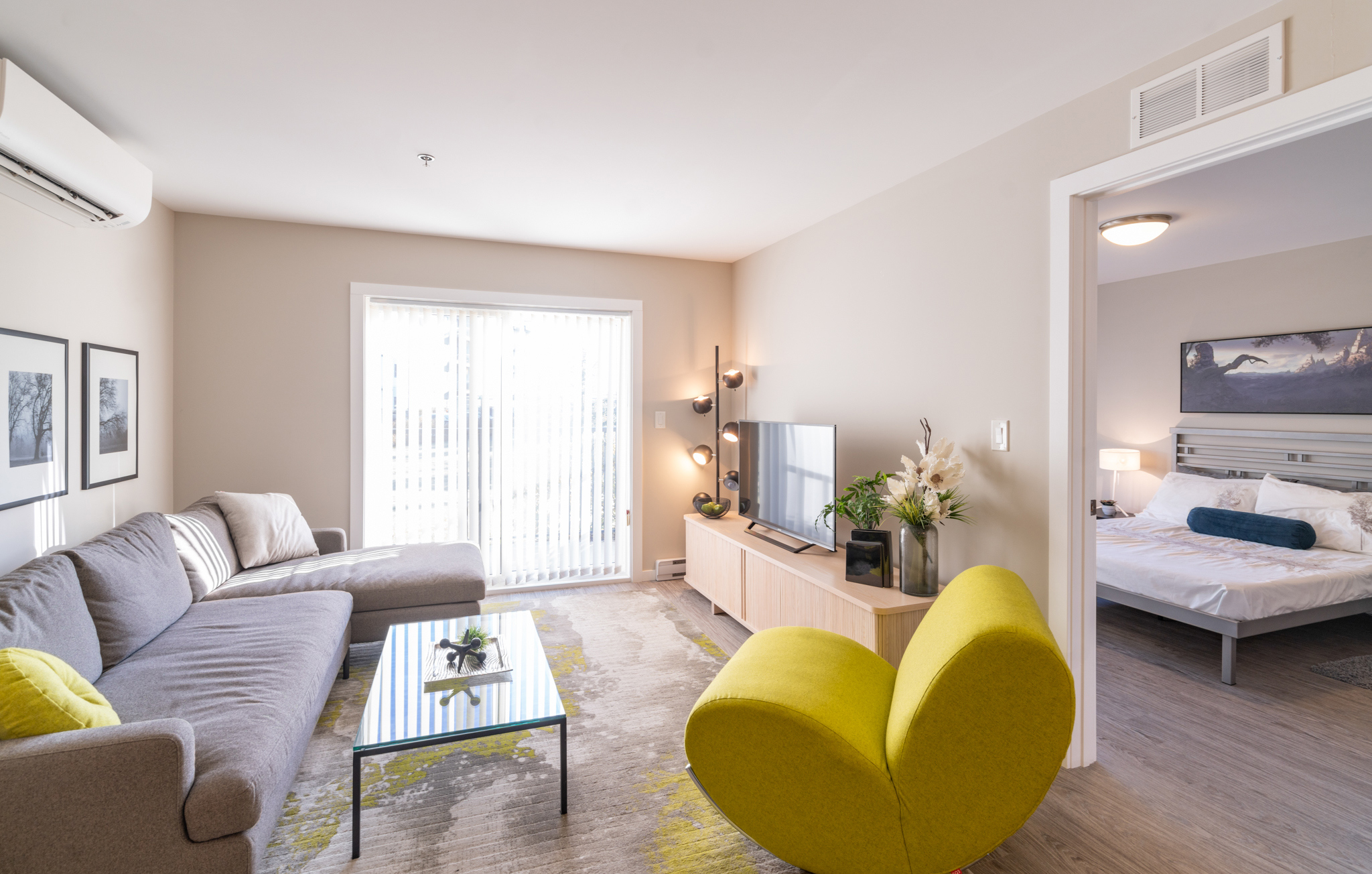 Image showing the interior of one of the suites. In the living room, there is a yellow armchair and a grey couch. Through a doorway, you can see into the bedroom.