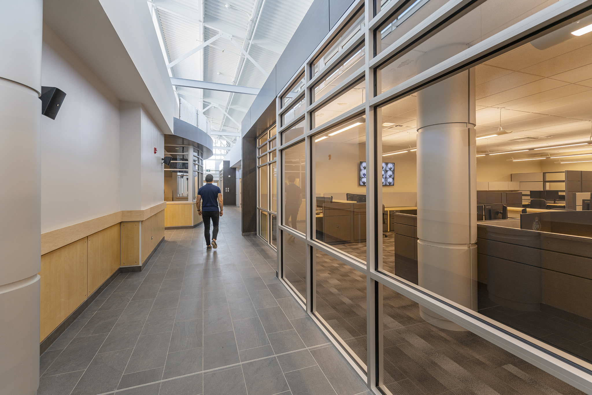 Image of a man walking down one of the station's hallways. Through the glass on the right side of the hallway, you can see desks and chairs of the office space.